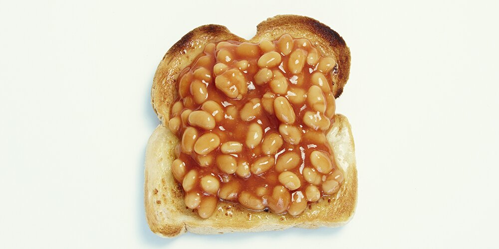 One piece of toast with baked beans on top. Studio lit and sitting on flat light surface.